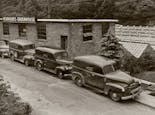 A line of early delivery trucks await product outside our greenhouse, circa 1930